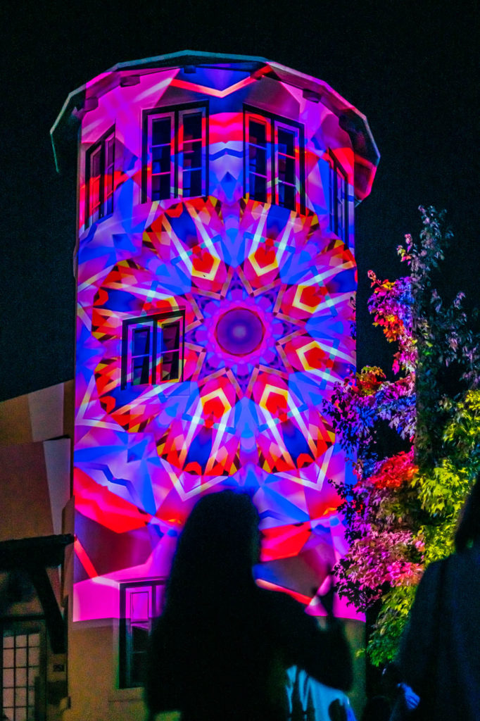 A home's corner tower lit up by a colorful light display.
