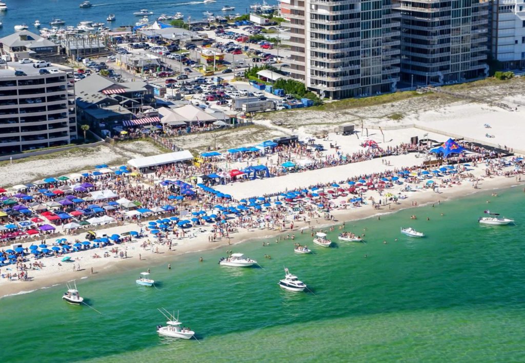 Aerial view of the beach beside Flora-Bama crowded with Mullet Toss partiers and boats.